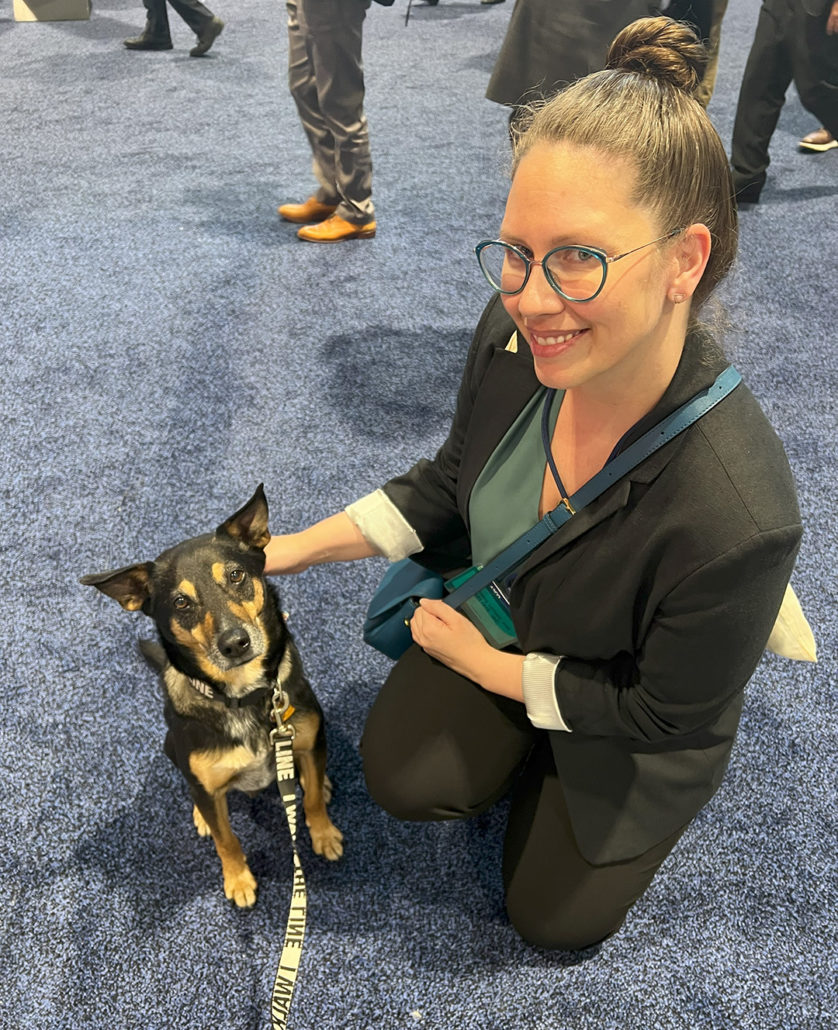 Photograph of a woman posing with a small dog in the exhibit hall of a scientific conference, ASCO 2024.