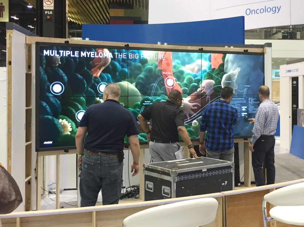 Photograph of AV technicians setting up and testing the multiple myeloma touch wall experience at ASCO 2017. AXS Studio team members are on hand to supervise and assist.