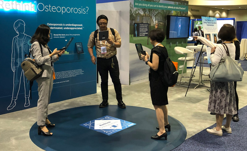 Participants using Rethink Osteoporosis at ASBMR 2019.  This is an augmented reality activity in which participants use an iPad to scan a virtual patient and her skeleton to find touchpoints. There are five touch points: hip; vertebra; wrist; humerus; clavicle. Tapping a touchpoint reveals information about fractures at that location and a question intended to spark discussion with an RML. This activity debuted at ASBMR 2019 in Orlando, FL.